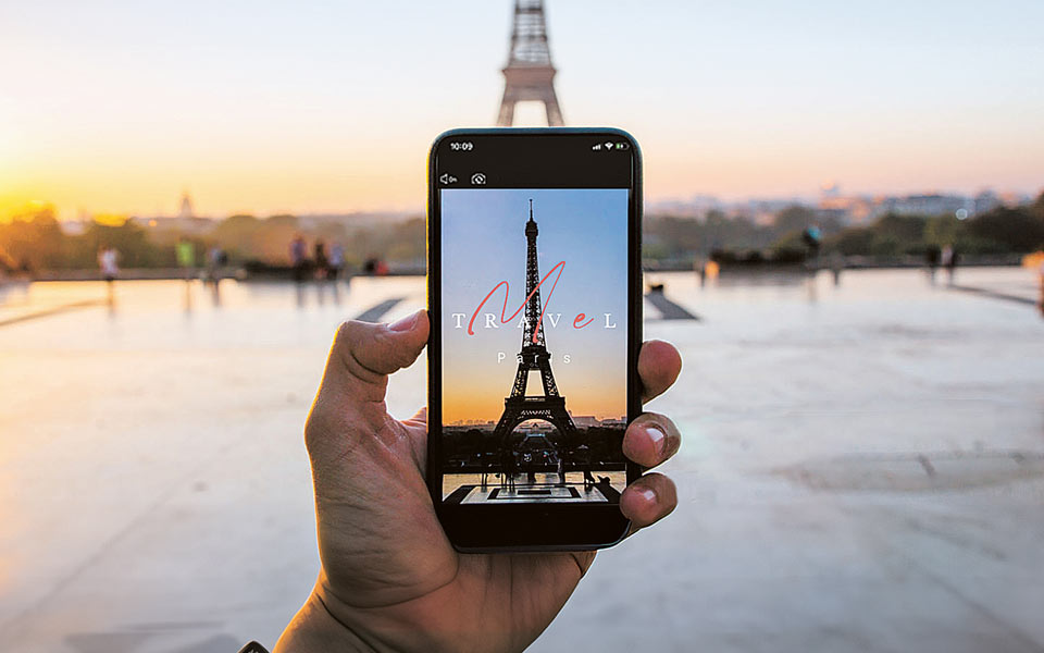 Personne tenant un smartphone prenant une photo de la Tour Eiffel, avec la Tour Eiffel réelle en arrière-plan au coucher du soleil