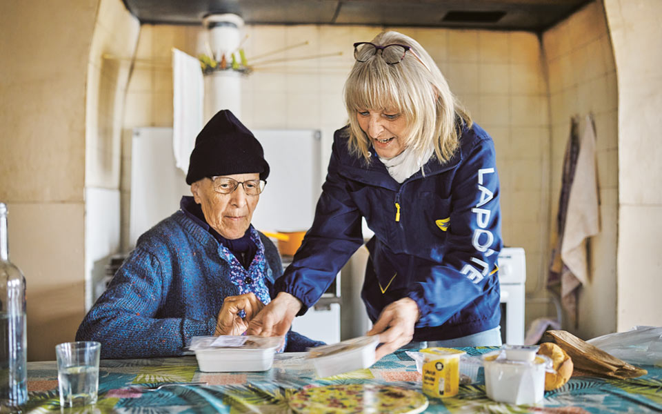 Factrice de La Poste apportant des repas à une personne âgée assise à une table