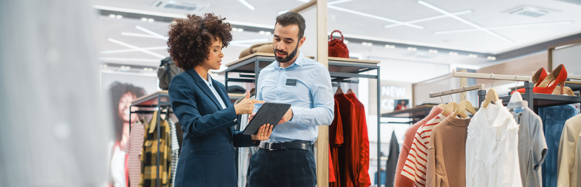 Magasin de vêtements : Une femme d'affaires utilise une tablette électronique, s'entretient avec un spécialiste du marchandisage visuel et collabore à la création d'une collection élégante. Le directeur des ventes d'une petite entreprise de mode s'entretient avec un styliste.