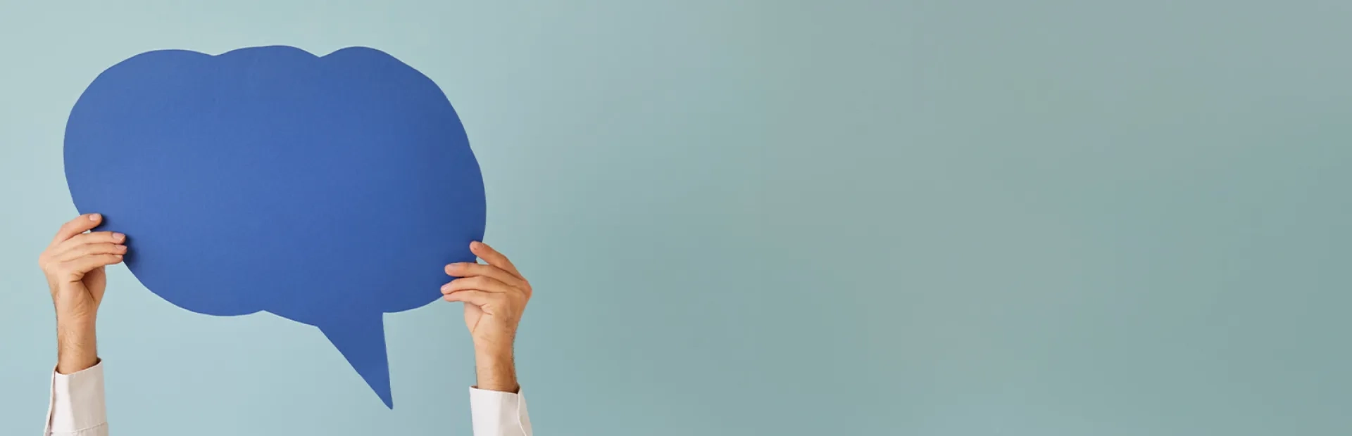 Deux mains tenant une grande bulle de dialogue bleue découpée sur un fond bleu clair.