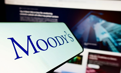 Téléphone portable avec le logo de l'agence de notation Moody's Investors Service Inc. à l'écran devant un site web d'entreprise. Focus sur la gauche de l'écran du téléphone