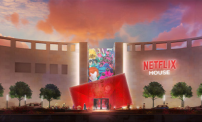 Illustration d'un bâtiment moderne nommé 'Netflix House', avec une façade lumineuse et artistique, un panneau Netflix visible, entouré de végétation et illuminé par un ciel coloré au coucher du soleil."