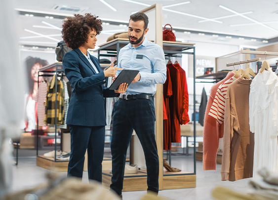 Magasin de vêtements : Une femme d'affaires utilise une tablette électronique, s'entretient avec un spécialiste du marchandisage visuel et collabore à la création d'une collection élégante. Le directeur des ventes d'une petite entreprise de mode s'entretient avec un styliste.