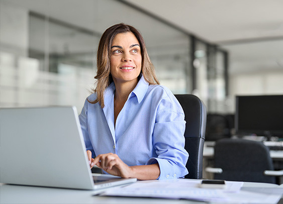 Femme d'affaires d'âge moyen, regardant au loin, travaillant sur un ordinateur portable dans un bureau, pensant à l'avenir des technologies de l'information et de la communication.