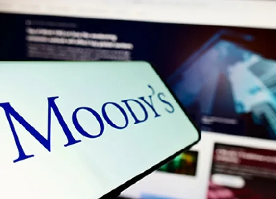 Téléphone portable avec le logo de l'agence de notation Moody's Investors Service Inc. à l'écran devant un site web d'entreprise. Focus sur la gauche de l'écran du téléphone